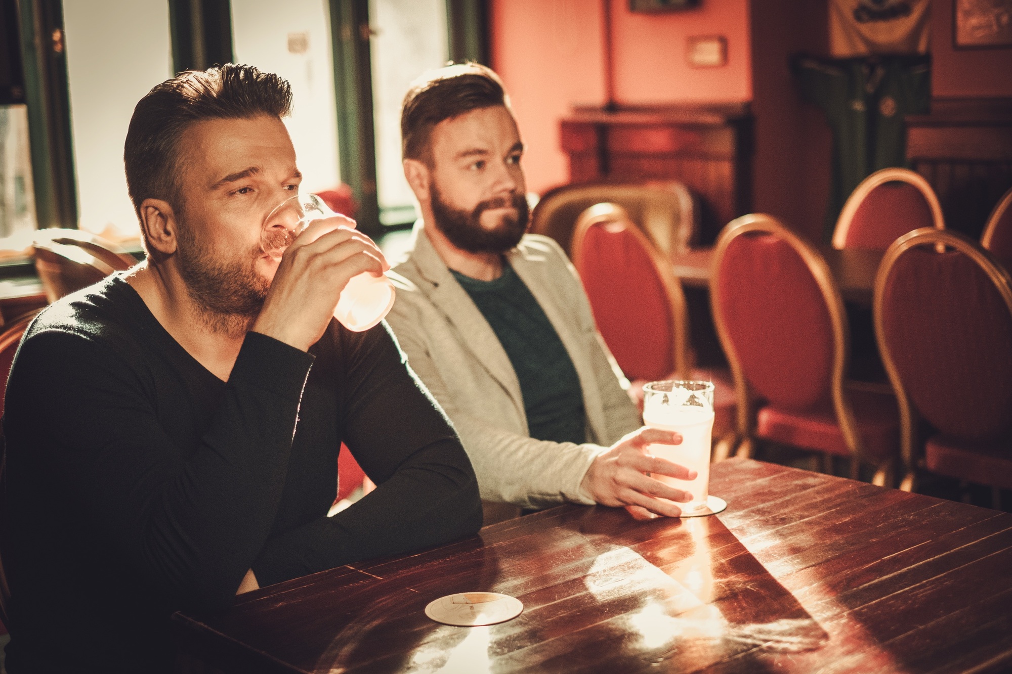 Friends watching TV and drinking draft beer in pub.